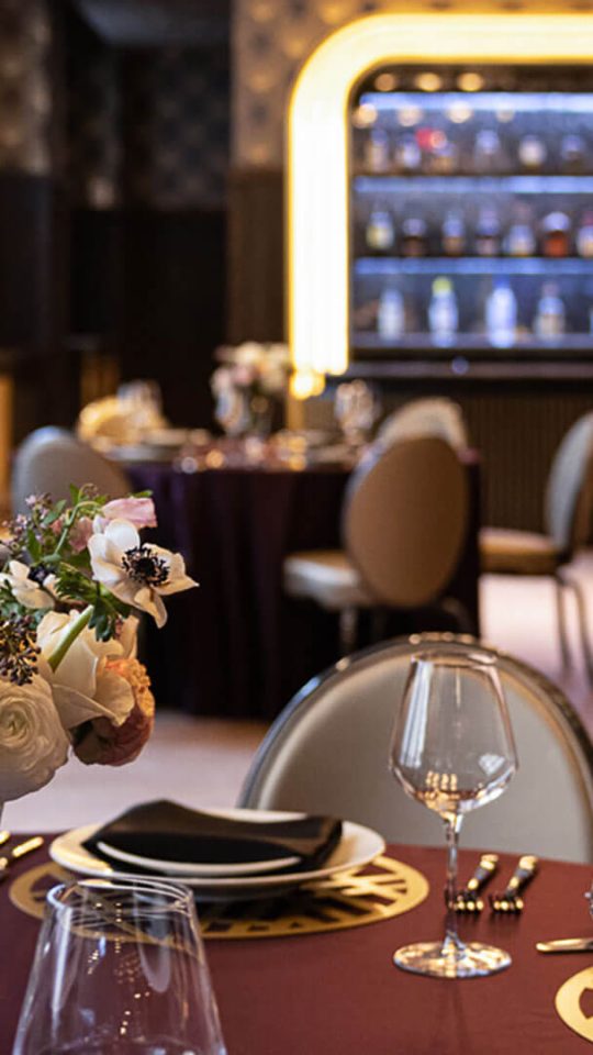 a restaurant setting with purple table cloths and wine glasses at The  First