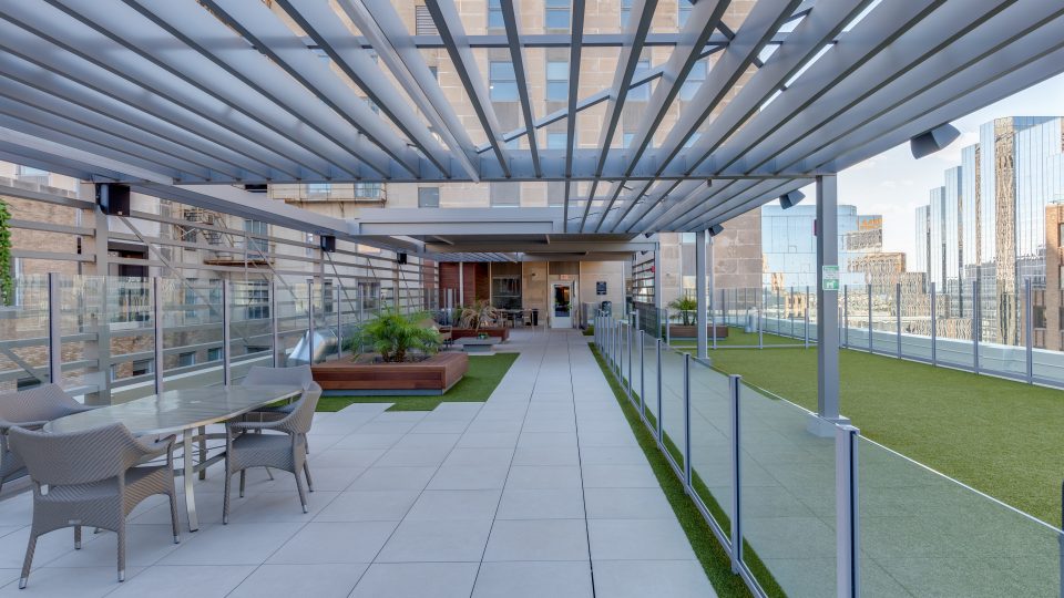 a rooftop patio with a pergolized roof and artificial turf at The  First