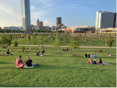 people are sitting on the grass in a Scissortail park near The First