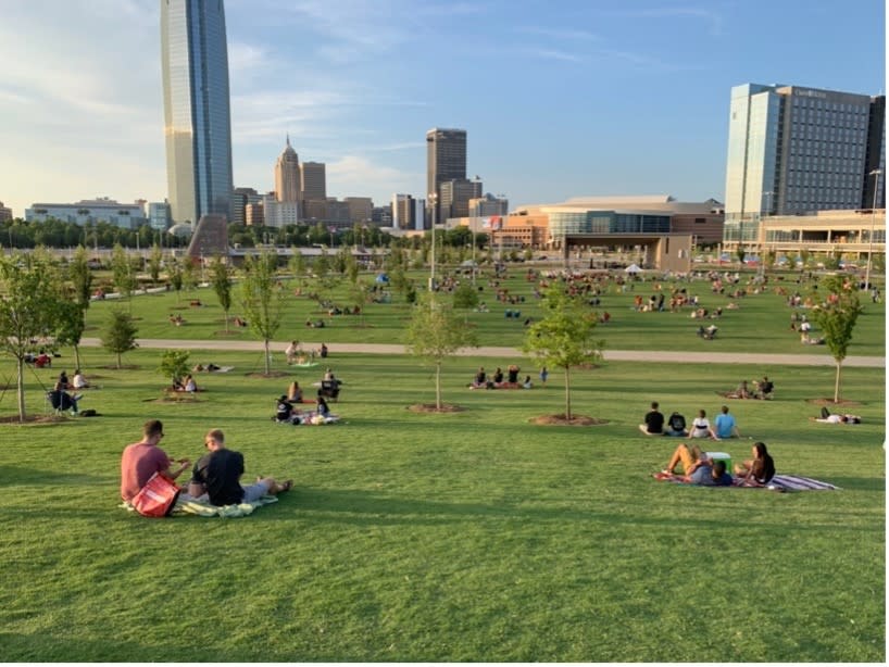 people are sitting on the grass in a Scissortail park near The First